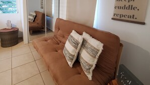A living room with a brown sofa, two pillows, a small round table with a decorative item, a wall-mounted sign with a motivational message, and a sliding glass door leading to another room. - Comfy apartment 8 minute walk from beach (Aguadilla)