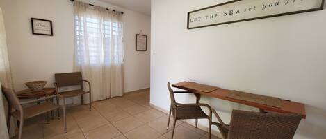 Una habitación con una mesa de comedor, sillas, un ventanal con cortinas y un cartel en la pared.
