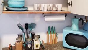 A kitchen with shelves holding glassware, plates, and bowls. There is a coffee maker and a microwave on the counter. - Comfy apartment 8 minute walk from beach (Aguadilla)