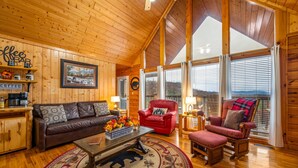 L’intérieur chaleureux d’un chalet avec un plafond en bois, un canapé en cuir, un fauteuil rouge et un coin bar.
