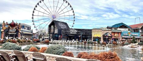 A waterfront area with a Ferris wheel, outdoor seating, and various shops.
