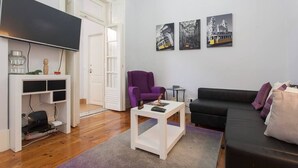 Una sala de estar moderna con un televisor de pantalla plana, un sillón púrpura, un sofá negro y una mesa de centro. Hay tres cuadros enmarcados en la pared.