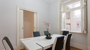Un comedor con mesa blanca, sillas negras y una orquídea en maceta.