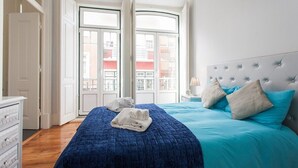Un dormitorio con una cama grande, un tocador y vistas a edificios a través de un ventanal.