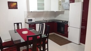 A compact kitchen with white cabinets, a microwave, a stove, and a refrigerator. There is a dining table with chairs and a red table runner. - Big apt with large terrace & great sea view, close to the beach (Arbanija)