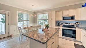 A kitchen with white cabinets, a granite countertop, stainless steel appliances, and a dining area with a table and chairs.
