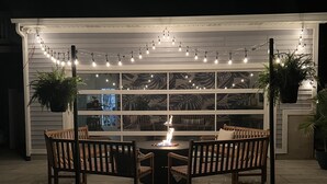 Patio esterno con tavolo rotondo e quattro sedie, circondato da luci a tenda e piante in vaso.