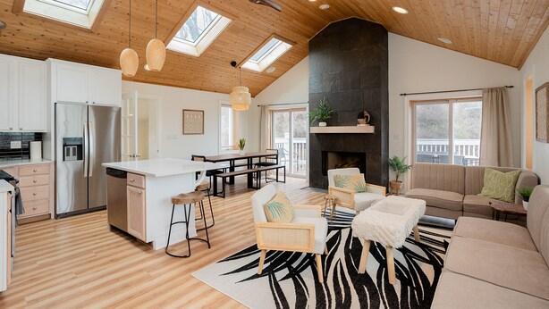 Un'ampia zona giorno con un grande camino, soffitto in legno e una cucina dotata di elettrodomestici moderni.