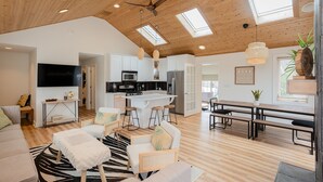 Un'ampia zona giorno con soffitto in legno, una cucina con mobili bianchi e un'area pranzo con panche.
