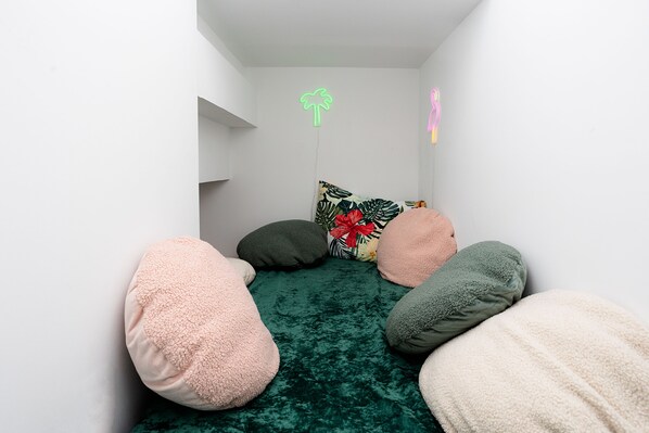 A cozy room with a green velvet bedspread, multiple fluffy pillows, and a neon palm tree sign on the wall. - Cabana style vacation home, w/HOT TUB & easy stroll to beach, sleeps 16. (Michigan City)
