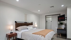 Habitación de hotel moderna con cama, mesitas de noche, escritorio y televisión mostrando el logotipo de Netflix.