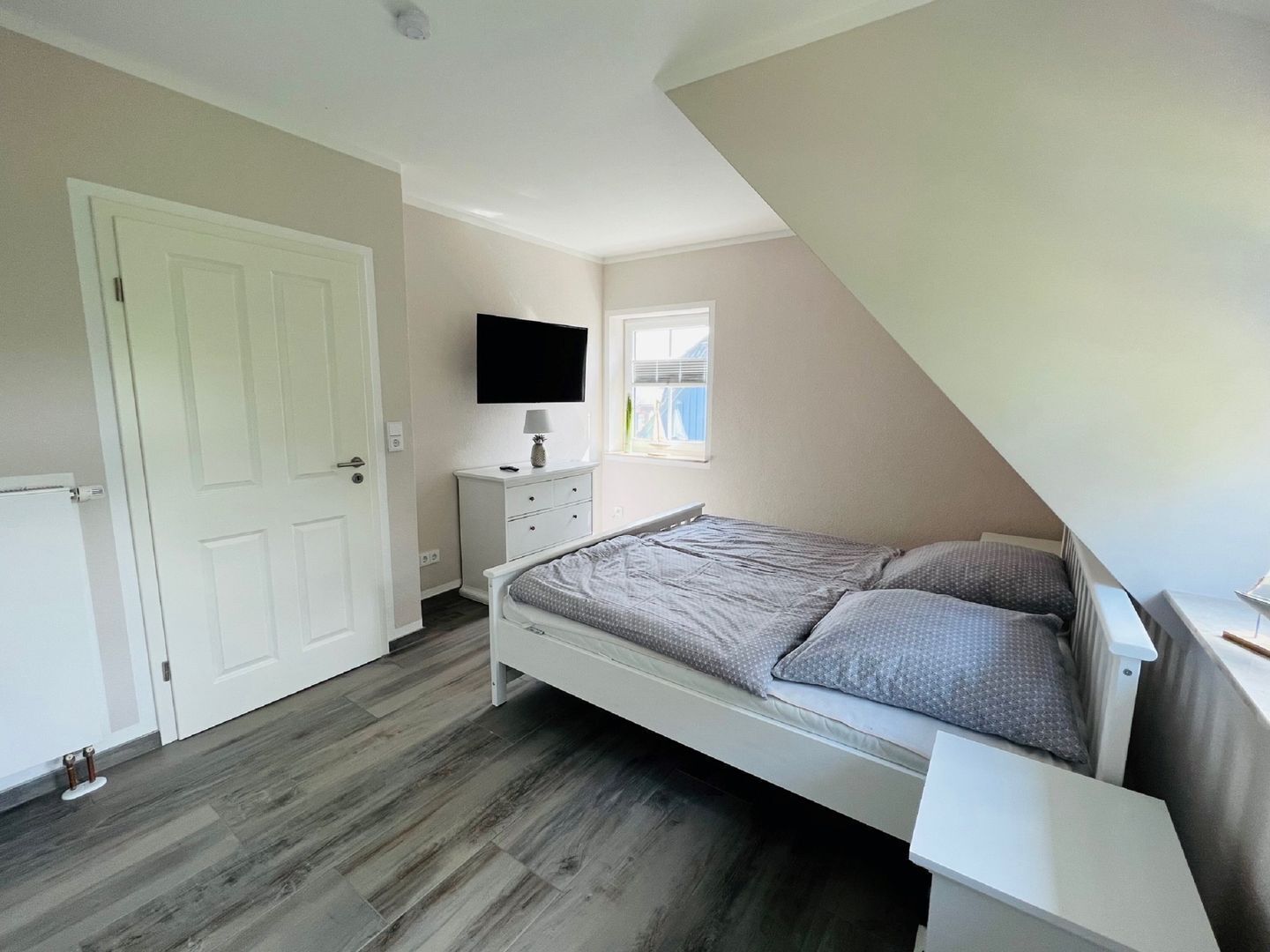 Un dormitorio con cama, televisión, cómoda y ventana.