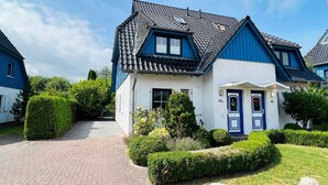 Ett tvåvåningshus med en blå och vit fasad, ett tegeltak och en välskött trädgård med häckar och en gång som leder till entrén.