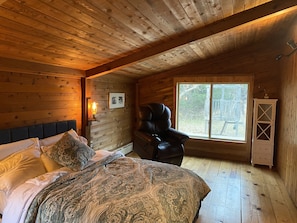 Un dormitorio acogedor tipo cabaña con una cama, un sillón de cuero, una ventana y un armario.