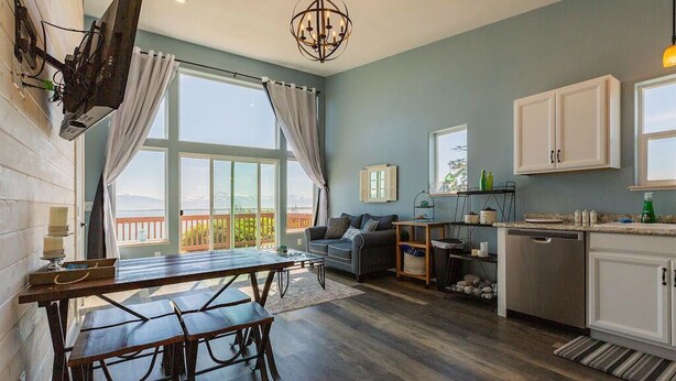 A modern kitchen with a dining area, large windows, and a view of a balcony. - Oceanfront Luxury Apartment Overlooking Kachemak Bay and Homer Spit! (Homer)
