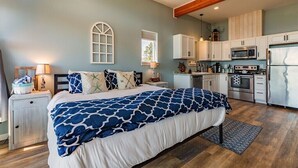 A bedroom with a large bed, a nightstand, a lamp, and a window. - Oceanfront Luxury Apartment Overlooking Kachemak Bay and Homer Spit! (Homer)