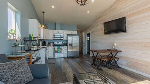 A modern kitchen with white cabinets, stainless steel appliances, and a dining area with a wooden table and chairs. - Oceanfront Luxury Apartment Overlooking Kachemak Bay and Homer Spit! (Homer)