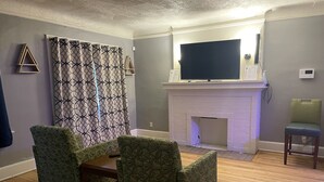 Een woonkamer met gestreepte fauteuils, een open haard en een flatscreen televisie.