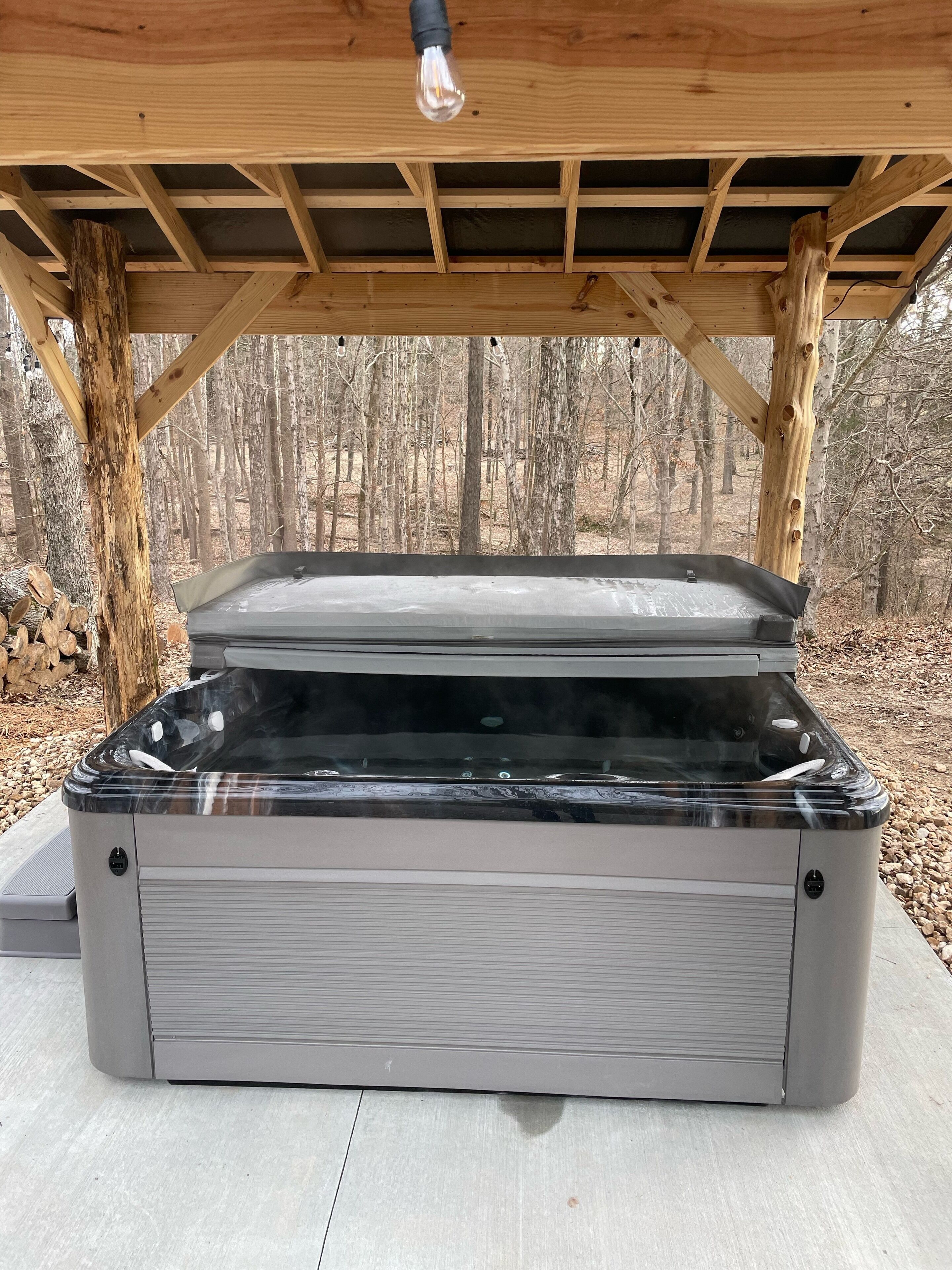 A hot tub under a wooden pergola with a view of a forested area.