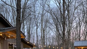 A building with a covered patio area, surrounded by trees and a gravel path.
