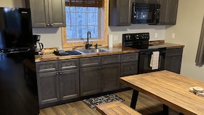 A modern kitchen with dark cabinets, a wooden countertop, a black refrigerator, a microwave, and a wooden dining table with benches.