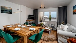 Un salon moderne avec une table à manger en bois, disposée pour quatre personnes, un canapé gris et un téléviseur posé sur un meuble.