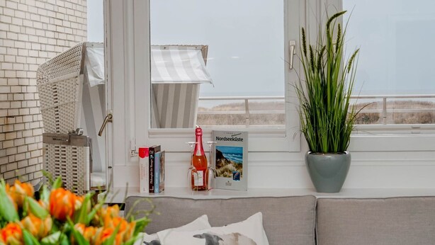 Une pièce confortable avec vue sur la mer, une bibliothèque remplie de livres, une bouteille de vin et une plante en pot.