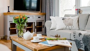 Un salon moderne avec une table basse en bois, un téléviseur à écran plat, un canapé agrémenté de coussins décoratifs et un vase de fleurs.
