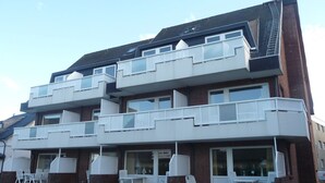 A multi-story residential building with balconies, a patio area with outdoor seating, and a brick facade. - Vacation apartment Mare Nostrum 6 - close to the beach, close to the city, close to relaxation, in short - (Sylt)