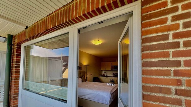 A room with a bed, a small kitchenette, and a sliding glass door leading to a balcony. - Vacation apartment Mare Nostrum 6 - close to the beach, close to the city, close to relaxation, in short - (Sylt)