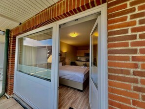 A room with a bed, a small kitchenette, and a sliding glass door leading to a balcony. - Mare Nostrum 6 Vacation Apartment—close to the beach, close to town, close to relaxation—in short— (Sylt)