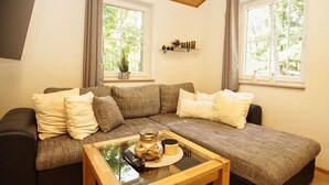 Una sala de estar acogedora con un sofá modular, una mesa de centro de vidrio y dos ventanas con cortinas.