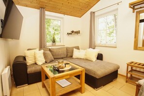 Un salón acogedor con un sofá modular, una mesa de centro de madera y un televisor montado en la pared.