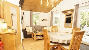 Un espacio de sala acogedor con un sofá, una mesa de comedor con sillas, vigas de madera en el techo y una ventana con vista a la vegetación.