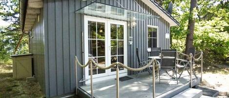 A small, single-story building with a glass door entrance, a covered outdoor seating area, and a rope barrier.