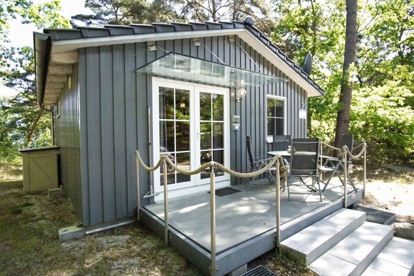 A small, single-story building with a glass door entrance, a covered outdoor seating area, and a rope barrier.