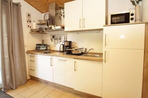 Una cocina compacta con armarios blancos, microondas, tostadora y cafetera.