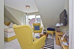 A modern hotel room with a bed, a yellow armchair, a small wooden table, a TV, and a window with a view of buildings. - Just 100 m from the beach, apartment with a balcony and private sauna - Apt. Eldena Vacation Rental 09 - (Middelhagen)