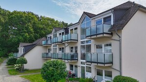 Ein mehrstöckiges Wohngebäude mit Balkonen, einer gepflasterten Auffahrt und umliegender Bepflanzung.