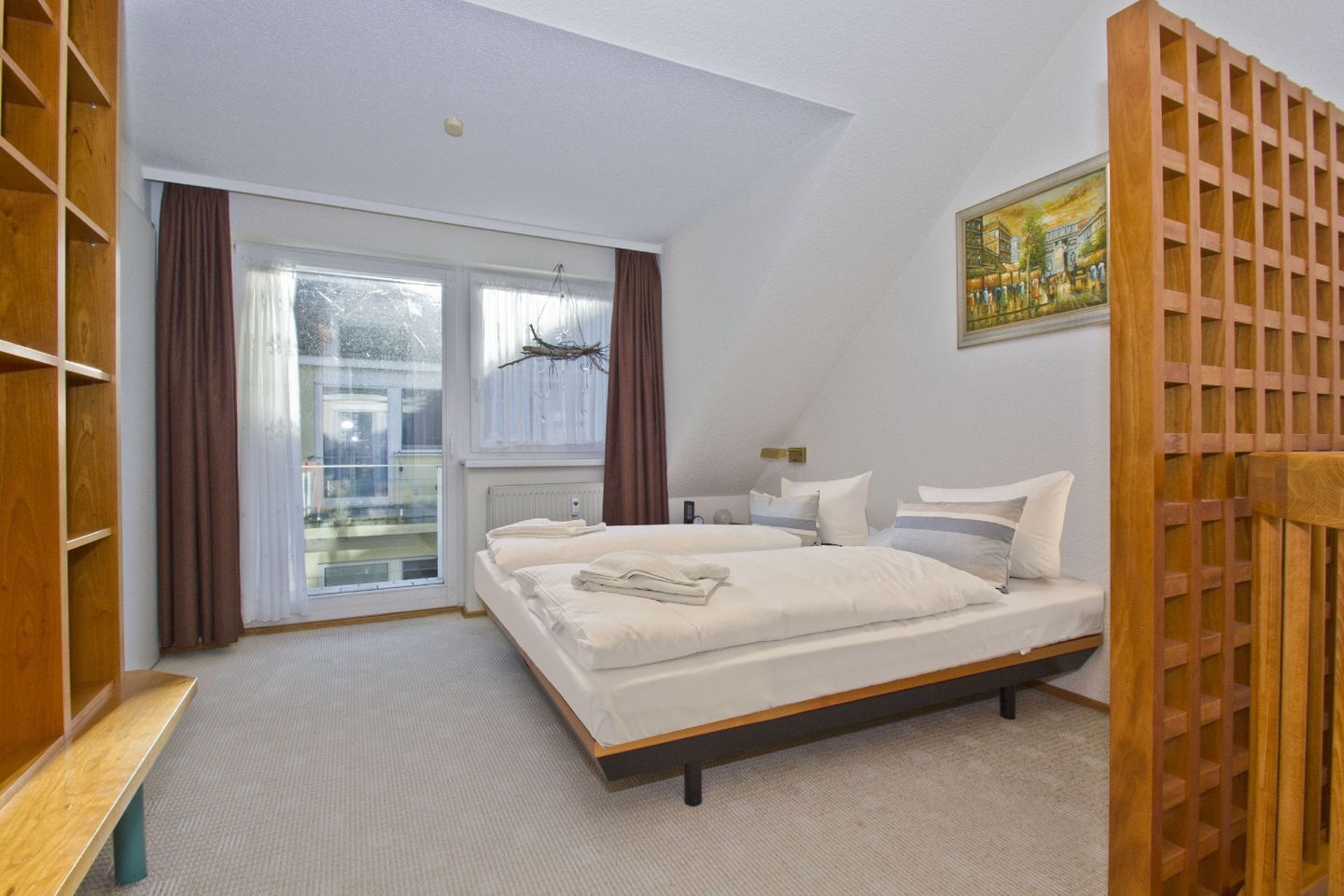 A bedroom with a large bed, a wooden wardrobe, a bench, a radiator, and a window with curtains.
