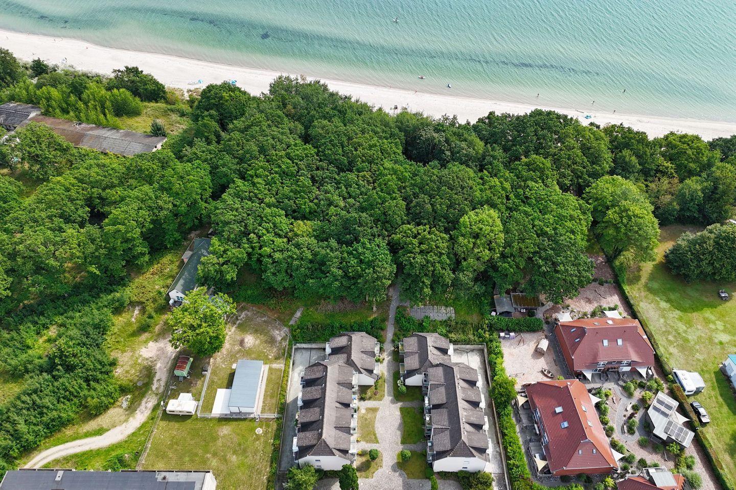Vue aérienne d’un quartier résidentiel avec une plage, une végétation luxuriante et de nombreuses maisons.