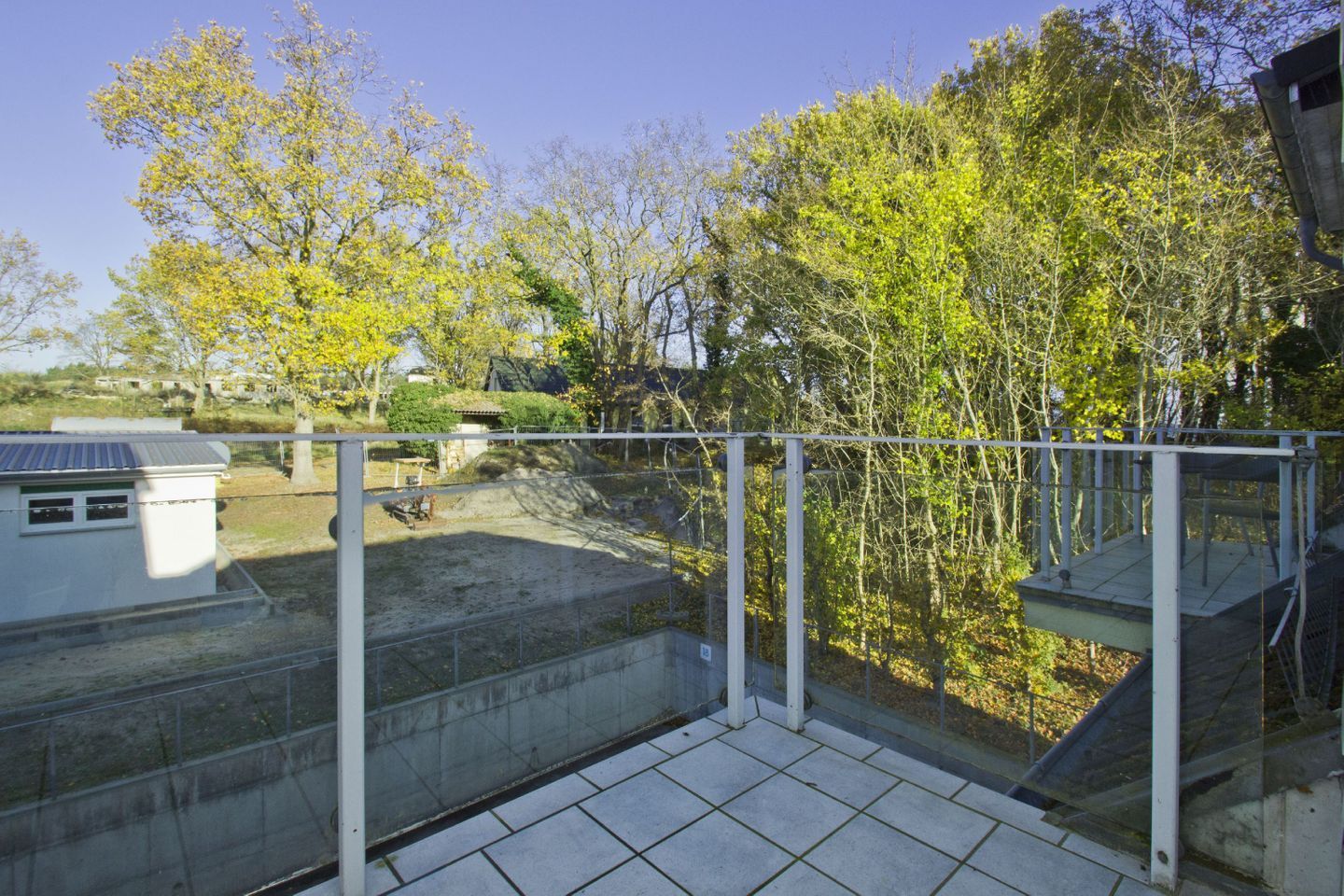 Un balcon donnant sur des arbres, avec un bâtiment visible au loin.