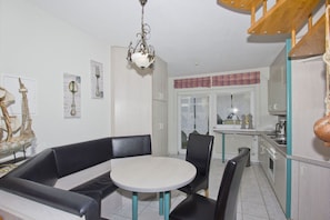 A dining area with a round table and black leather seating, a kitchen with white cabinets and a window with plaid curtains, and a decorative ceiling light. - Just 100 m from the beach, apartment with a balcony and terrace - Apt. Eldena Apartment 19 - (Middelhagen)