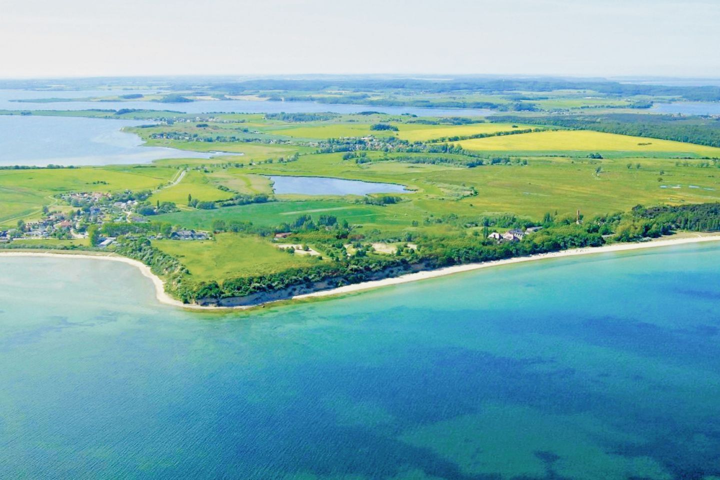 Vue aérienne d’une zone côtière avec une plage, des champs verdoyants et un petit village.