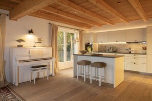 A modern kitchen with white cabinetry, a piano, and a bar area with stools.