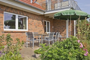 Une maison en briques avec un balcon, une terrasse avec une table et des chaises, et un jardin fleuri.