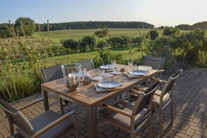 An outdoor dining table set up with chairs, plates, glasses, and a candle holder, overlooking a green field.