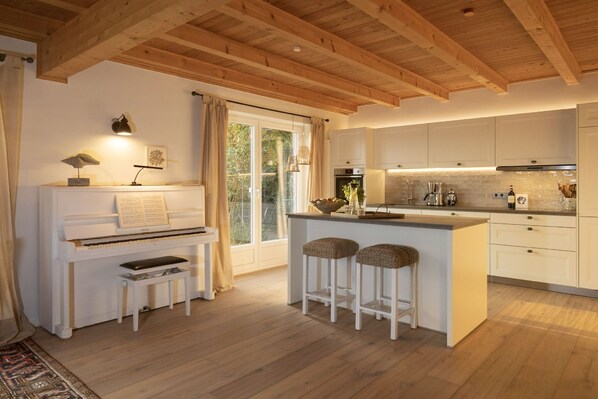 A modern kitchen with white cabinetry, a piano, and a bar area with stools.