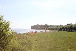 A grassy field with a beach, tents, and trees.