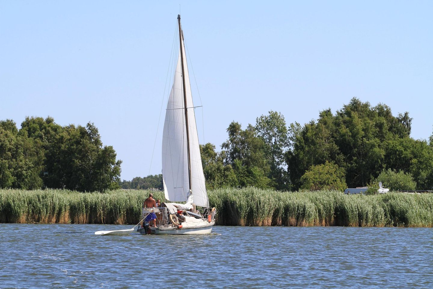 A sailboat on a calm river with a forested bank in the background.